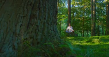 Solunum sistemini onarmak için nefes egzersizleri. Güzel bir kadın ormanın ortasında yerde oturarak meditasyon yapıyor. Genç bir kadın gözleri kapalı ormanlık alandan zevk alıyor. Yavaş çekim