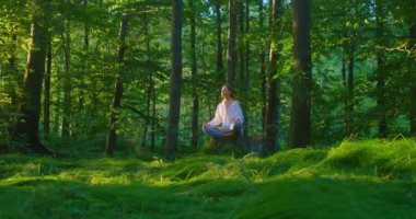 Doğayla birlik. Dinginlik ve tefekkür. Dünya Akıl Sağlığı Günü. Güzel bir kadın ormanın ortasında yerde oturarak meditasyon yapıyor. Solunum sistemini eski haline getirmek için nefes egzersizleri
