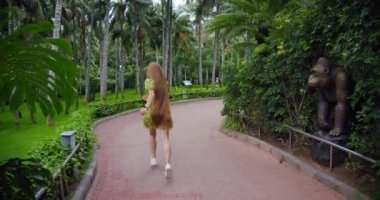 Parkta koşuşturan mutlu bir kadının silüeti. Kısa yeşil elbise ve rüzgarda yavaşça çırpınan uzun saçlar. Bir turist tatilin tadını çıkarıyor. Video görüntüleri 4K.
