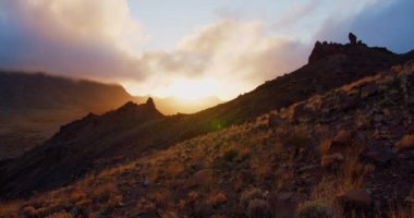 Manzaralı dağ sıralarının üzerinde güzel bir gün batımı manzarası. Altın saat, Tenerife 'deki Teide Ulusal Parkı' nın üzerindeki bulutlar, Kanarya Adası, İspanya. ön plandaki yerel bitki örtüsünde.