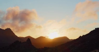 Gün batımında ya da şafakta yüksek ıssız dağlar. Güneş ışınları kayaları aydınlatır. Arka planda bulutlu renkli gökyüzü. Tenerife 'deki Teide Ulusal Parkı. Kanarya adaları.