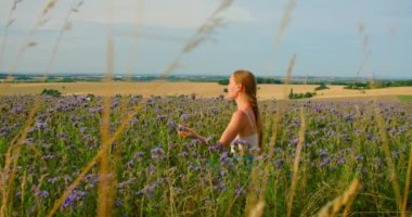 Young long-haired woman on purple flowers field meditating. Calm face, eyes closed, inhaling and exhaling aromas. Happiness against blue sky sunset in summer, enjoys nature slow motion. Aromatherapy
