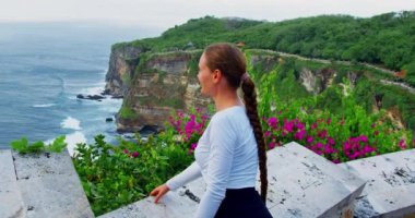 Woman tourist sightseeing cliff landscape with ocean view Uluwatu Temple Pura Luhur Hindu on Bali Island Indonesia. Rear view of girl in tropical country during vacation. Travel destination.
