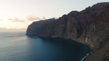 Colorful sunset light over ocean water, waves crash on rocky mountain beachfront. Aerial sun set above cliffs silhouette. Tropic nature seascape. Paradise island Tenerife Spain. Cinematic drone shot