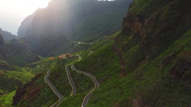 Mountain village Masca in ravine during foggy spring morning. Green hills landscape with sun glare. Famous tourist destinationTenerife Canary Islands Spain Europe. Aerial drone flight.