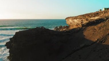 Gün batımında mavi Atlantik Okyanusu suyuyla birlikte kayalık sahil şeridinde. Doğa manzarası. Altın kumtaşı blöf plajı. Seyahat güzergahı. Fuerteventura Adası, Kanaryalar. 4K sinematik görünüm