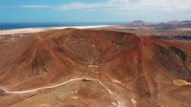 Drone flight over deserted landscape near to town Corralejo. Hiking path to volcanic empty Las Calderas, Caldera Encantada. Fuerteventura, Canary Island, Spain. Blue ocean. Cityscape. Cloudscape