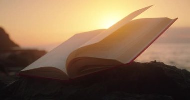 Open book on beach at sunset light. Ocean on the background.