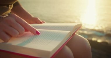 Woman reading book on beach at sunset light. Learning, studying, education concept. Blurred ocean water on background.