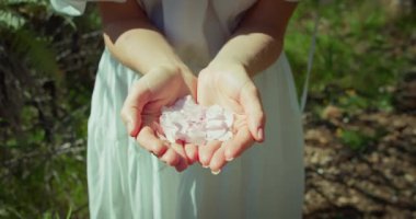 Kapalı alanda çiçek yaprakları olan dişi avuçlar. Bir kadın, avuçlarındaki leylak çiçeklerinin yapraklarını bir bahar parkının arka planına savuruyor. Yavaş çekim.