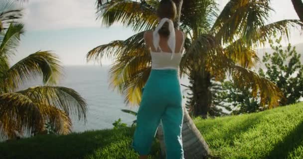 在阳光明媚的夏日 大自然的情人 成年姑娘在热带森林里散步 抱着一棵棕榈树 沉浸式旅行的概念 快乐的女人微笑着欣赏着海滨的落日 — 图库视频影像