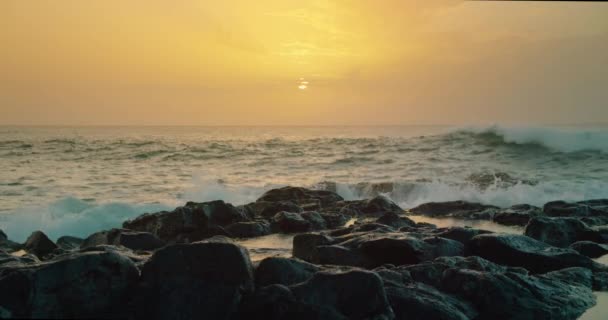 海の波は 地平線上の沈む太陽を覆う海岸で衝突します 日没時に近くの岩の多いビーチの嵐の海 水噴霧泡だ 巨大な危険な波が海岸の岩を破る 禅瞑想の背景 — ストック動画