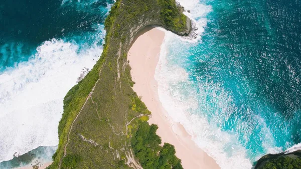 Kelingking sandy beach with tall overgrown rocky cliff Nusa Penida Island. Aerial top down view of best tourist destination in Indonesia Asia. Tropical ocean landscape.