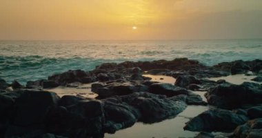 Okyanus dalgaları ufuktaki batan güneşi kaplayarak kıyıya çarpar. Gün batımında kayalık kumsal fırtınalı denizde. Su spreyi, köpük. Dev tehlikeli dalgalar kıyı kayalarını kırıyor. Zen meditasyon arkaplanı.