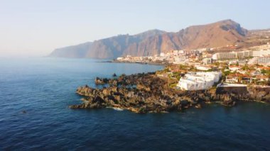 Güzel Tenerife Adası 'nın hava manzarası. Volkanik kayalık keskin plaj. Puerto de Santiago tatil köyünün etrafındaki tropik berrak mavi okyanus suları. Arka planda büyük dağ kayalıkları var. Kimse.