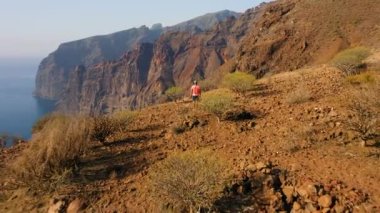 Tenerife Kanarya Adası, güzel dağlar, mavi okyanus manzarası. Tehlikeli bir turistik yer. Adam Los Gigantes 'in dik uçurumlarının kenarında duruyor. Hayati tehlikesi olan inanılmaz bir rota. Doğa manzarası