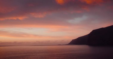Pembe gün batımı bulutlu gökyüzü, sakin okyanus suyunun üzerinde. Los Gigantes Tenerife 'deki kayalıklarda. Sakin alacakaranlık deniz manzarası. Kanarya Adaları İspanya Avrupa.