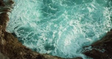 Kızgın okyanus dalgaları kayalık sahil şeridinde beyaz köpüklü suya yakın. Yavaş çekim sinematik tepeden aşağı görünüm.