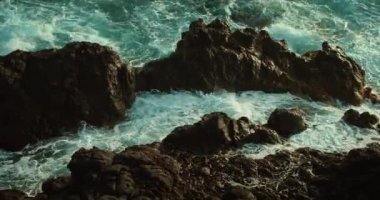 Okyanus dalgaları kayalık kıyıları yıkıyor. Kızgın deniz turkuazları köpüren ve yakın plan sinematik görüntüler saçan. Siyah volkanik kaya oluşumları..