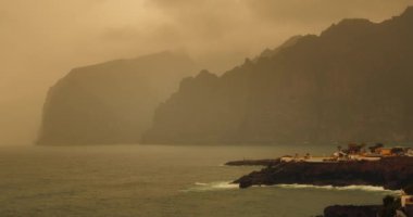 Sisli sarı duvak okyanustaki kayaları kapladı. Tenerife Los Gigantes 'te kum fırtınası. Kanarya Adaları Afrika Sahra kum fırtınası tarafından vuruldu. İspanya