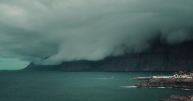 Ağır gri bulutlar karanlık okyanusta büyük kayaları kapladı. Fırtınadan önce hava. Craggy volkanik adası Tenerife, Los Gigantes uçurumları, Kanarya İspanya. Deniz manzarası üzerinde kasvetli bir gökyüzü.