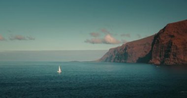İspanya 'nın Tenerife Kanarya Adası' ndaki dağların yakınındaki okyanus koyunda yapayalnız bir yat. Los Gigantes uçurumlarının yaz tatili manzarası, kayalık sahil.