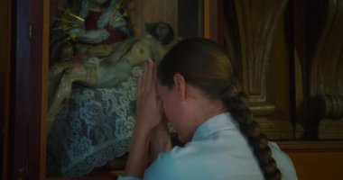 Hıristiyan kadın kilisede çarmıha gerilmiş İsa 'nın arka planına karşı diz çöküp dua ediyor. Tapınakta Tanrı 'ya tapan dindar bir kız. Yavaş çekim.