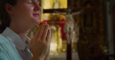 Huzurlu, mutlu, genç bir kadın kilisede Tanrı 'ya şükranla dua ediyor. Arka planda çarmıha gerilmiş İsa Mesih. Tapınakta yakın plan Hıristiyan kız yüzü