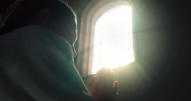 Kadın kilisede boyalı cam pencerenin yanında Tanrı 'ya dua ederken başını eğmiş. Kurtarıcı İsa 'ya dua etmek için katlanmış eller. Hıristiyanlık dini kavram.