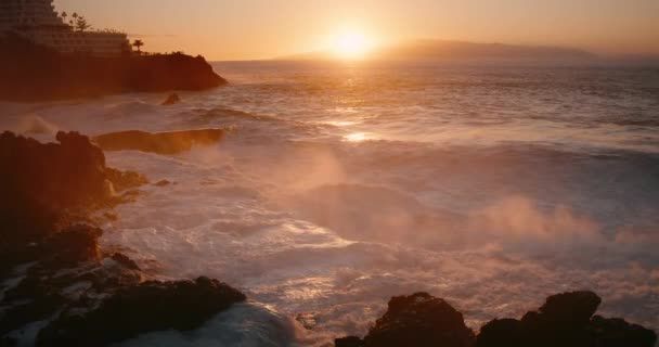 劇的な荒波は スローモーションで黄金の日没でプエルト サンティアゴ市の岩の海岸線で衝突します 海の水の空気中に高噴霧飛沫や桟橋のクローズアップを打つ テネリフェ島カナリア — ストック動画