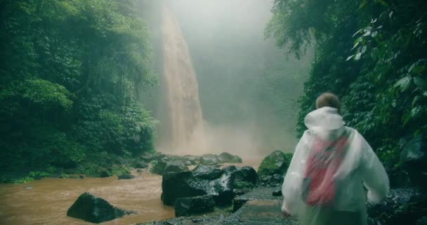 Женщина Путешественница Дождевом Плаще Наслаждается Тропическими Лесами Смотрит Мощный Водопад — стоковое видео