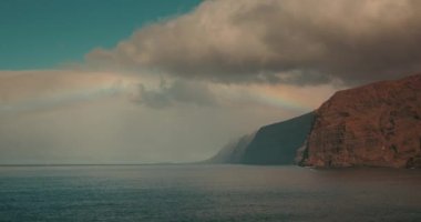 Karanlık okyanus manzarası ve gökyüzünde parlak gökkuşağı. Tenerife 'deki doğal olay, Los Gigantes uçurumları.