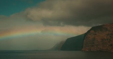 Karanlık okyanus manzarası ve gökyüzünde parlak gökkuşağı. Tenerife 'deki doğal olay, Los Gigantes uçurumları.