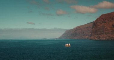 Turist ortaçağ korsan gemisi okyanusta yelken açar. Tenerife Kanarya Adaları 'ndaki devasa volkanik dağlar Los Gigantes kayalıkları. Kayalık sahillerin yaz tatili manzarası.