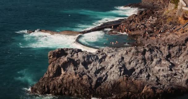 在特内里费加那利群岛 汹涌的海浪冲击着天然游泳池的岩石海岸 Charco Isla Cangrejo 难以辨认的游客度假时晒日光浴 — 图库视频影像