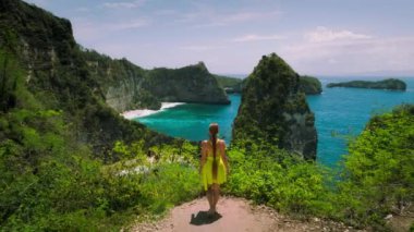 Elbiseli kız tatilde dağın kenarında yürüyor. Nusa Penida Bali Endonezya 'da beyaz kumlu ve dik kayalıkları olan elmas plajı.
