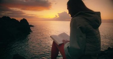 Tenerife 'de gün batımında Rocky Beach' te kitap okuyan bir kadın silueti..