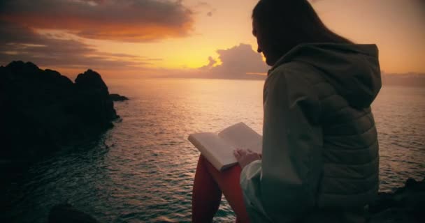 Γυναικεία Σιλουέτα Που Διαβάζει Βιβλίο Για Βραχώδη Παραλία Στο Ηλιοβασίλεμα — Αρχείο Βίντεο