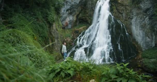 在奥地利高地享受瀑布的女旅行者 在山上旅行 冒险和旅行的概念 女孩在森林里凝视着大自然的美丽 — 图库视频影像