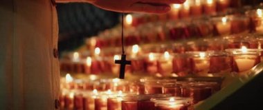 Kilisede dua eden bir kadın. Yetişkin bir kız yanan mumların yanında haçla el ele tutuşuyor. Doğal ateş ışığı.