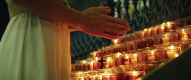 十字架を握り 寺院でろうそくの近くで祈っている女性 大人の少女は燃える炎の近くで罪のために熱心に手を折りました 自然な火のライトの背景 — ストック動画