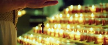 Kilisede dua eden bir kadın. Yetişkin bir kız yanan mumların yanında haçla el ele tutuşuyor. Doğal ateş ışığı.