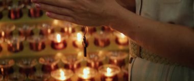 Tanrı 'nın Tapınağı' nda yanan mumların yanında tahta bir haç tutan kadın eller. Tanrı 'ya Hristiyan inancı.