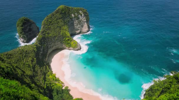 崖の上に濃い緑の森がある砂浜の熱帯の自然 山の風景とターコイズクリアな海の波 バリ島のヌサペニダケリングビーチの空中ビュー — ストック動画