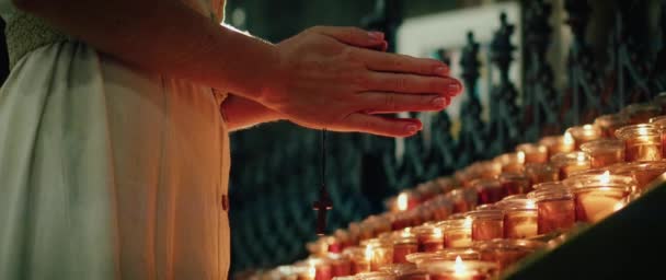 十字架を握り 寺院でろうそくの近くで祈っている女性 大人の少女は燃える炎の近くで罪のために熱心に手を折りました 自然な火のライトの背景 — ストック動画
