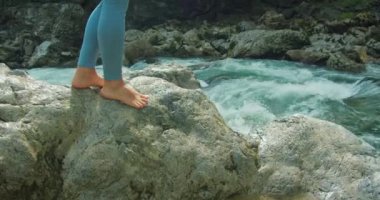 Çıplak ayaklı kız, kristal berrak suyla güçlü bir nehrin kıyısındaki kayalara tırmanıyor. Sağlıklı, güzel kadın bacakları. Yakın plan. Dağlarda yürüyüş parkurunda. Avusturya Hallstatt yakınlarında Lammerklamm Boğazı