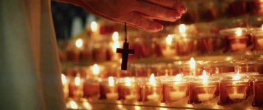 Tanrı 'nın Tapınağı' nda yanan mumların yanında tahta bir haç tutan kadın eller. Tanrı 'ya Hristiyan inancı.