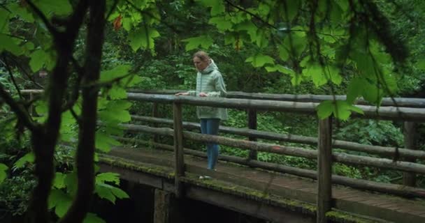 Vrouw Inspecteert Natuur Terwijl Een Houten Brug Staat Regenachtige Dagen — Stockvideo