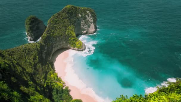 崖の上に濃い緑の森がある砂浜の熱帯の自然 山の風景とターコイズクリアな海の波 バリ島のヌサペニダケリングビーチの空中ビュー — ストック動画