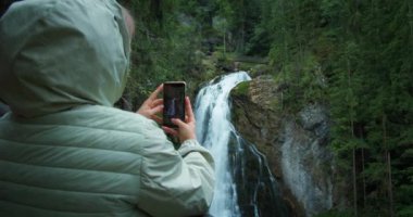 Kadın turist Avusturya 'daki Golling şelalesinin telefonunda fotoğraf çekiyor. Kızın arka görünüşü.